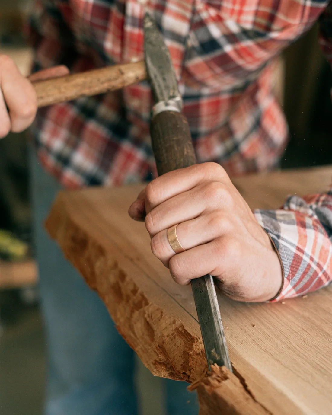 Handwerker bearbeitet einen Holzbalken mit Stemmeisen und Holzhammer