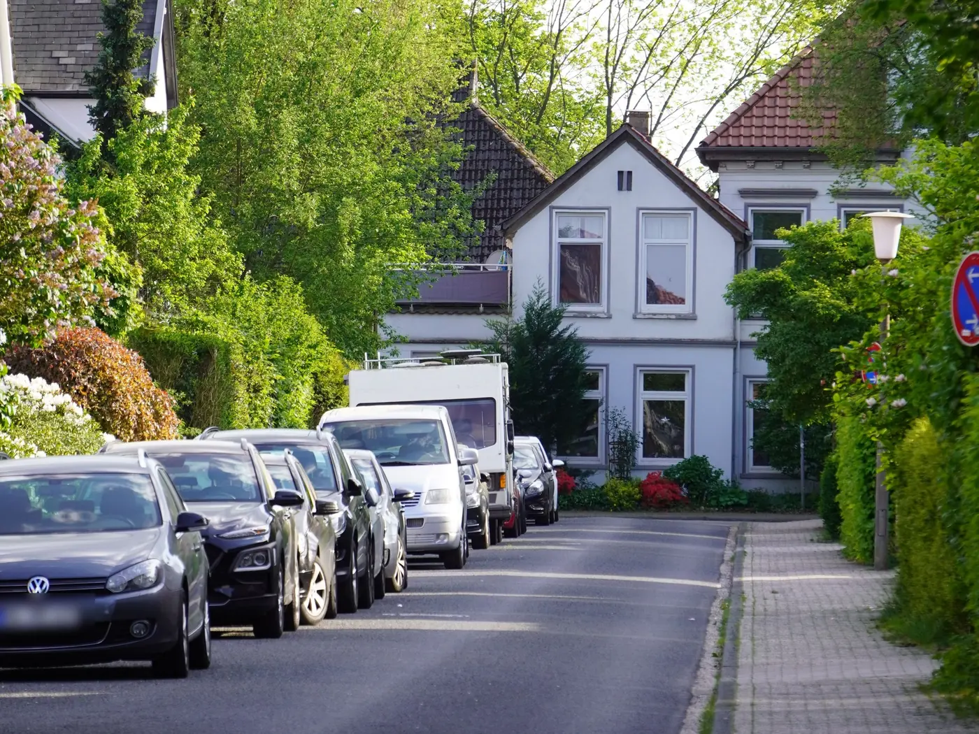 Ruhige Wohnstraße mit geparkten Autos, Hecken und Giebelhäusern