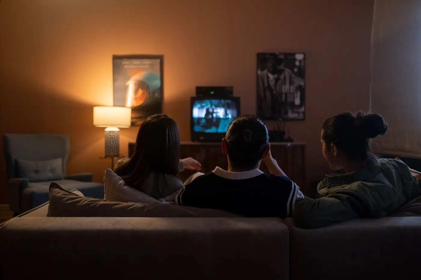 Drei Menschen sitzen abends auf dem Sofa vor einem laufenden Fernseher